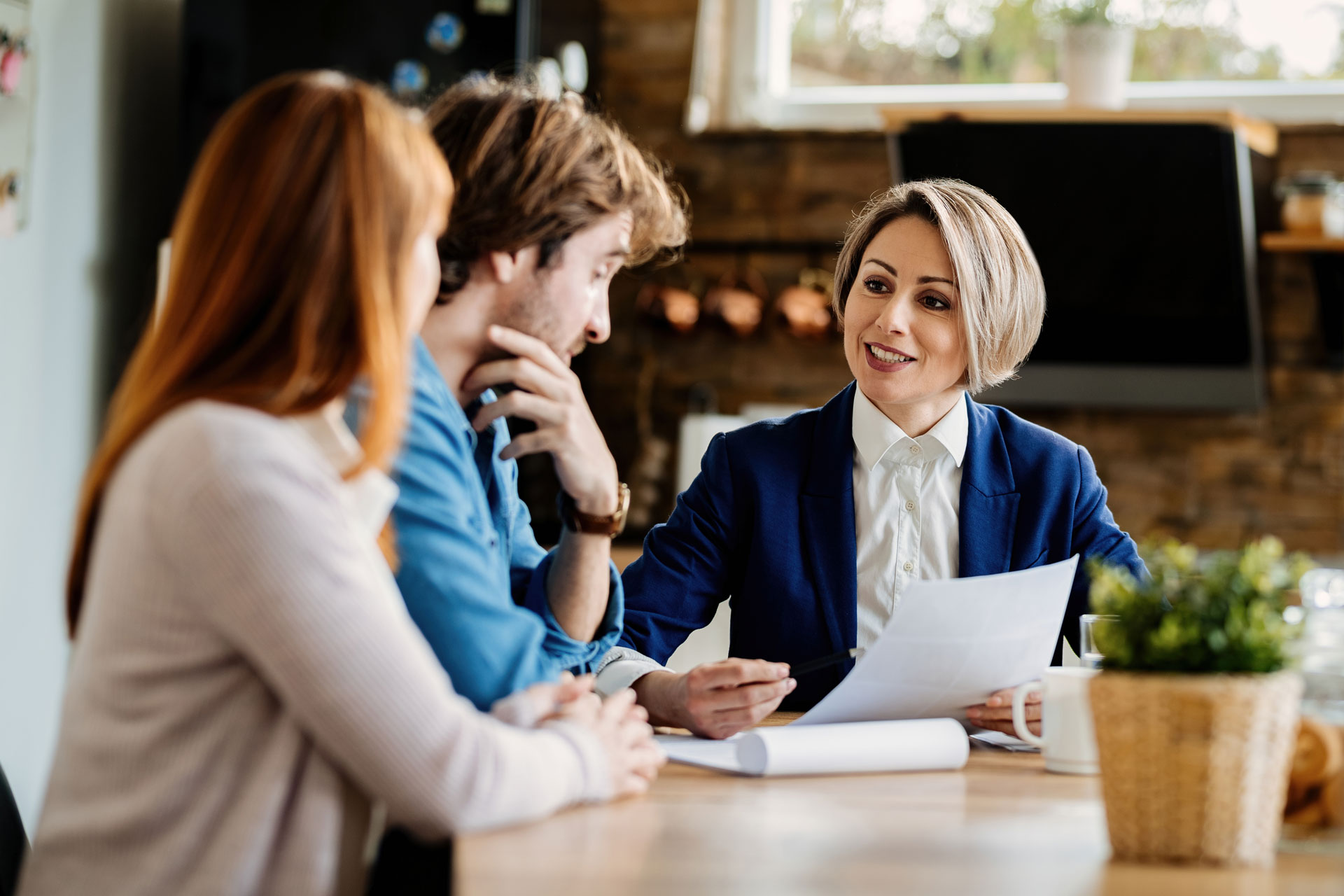 happy-financial-advisor-young-couple-communicating-while-going-through-paperwork-during-meeting